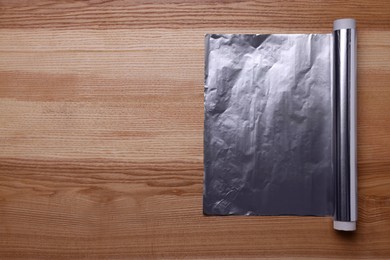 Roll of aluminum foil on wooden table, top view. Space for text