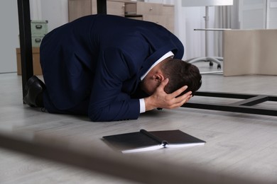 Photo of Scared man hiding under office desk during earthquake