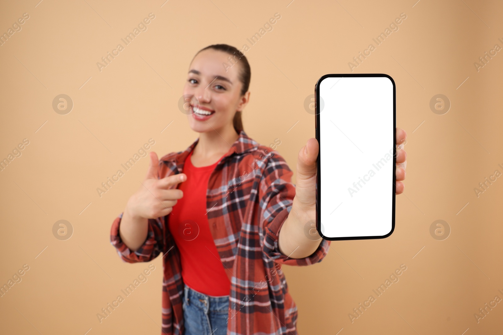 Photo of Young woman showing smartphone in hand and pointing at it on light brown background, selective focus. Mockup for design