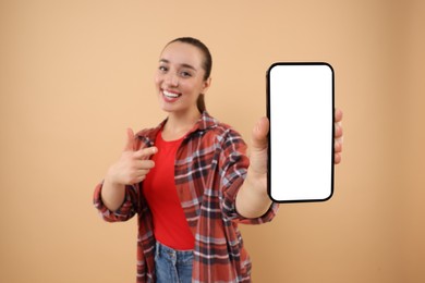 Young woman showing smartphone in hand and pointing at it on light brown background, selective focus. Mockup for design