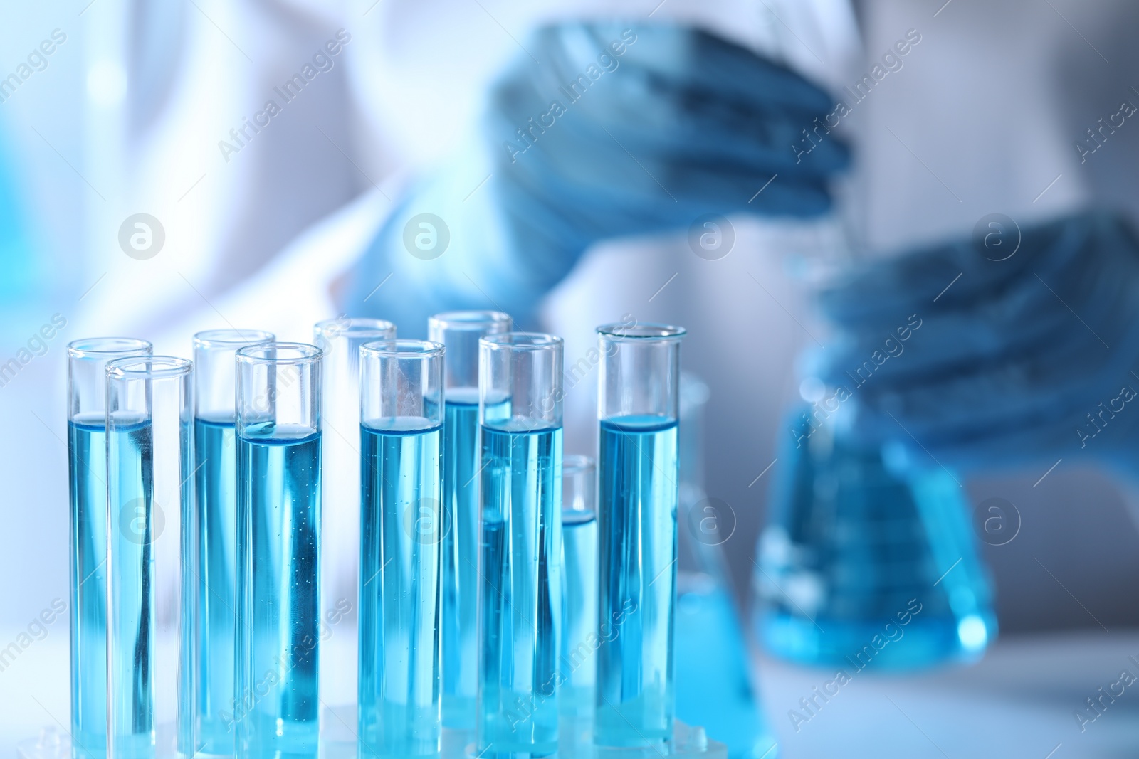 Photo of Scientist holding flask near test tubes with light blue liquid, selective focus