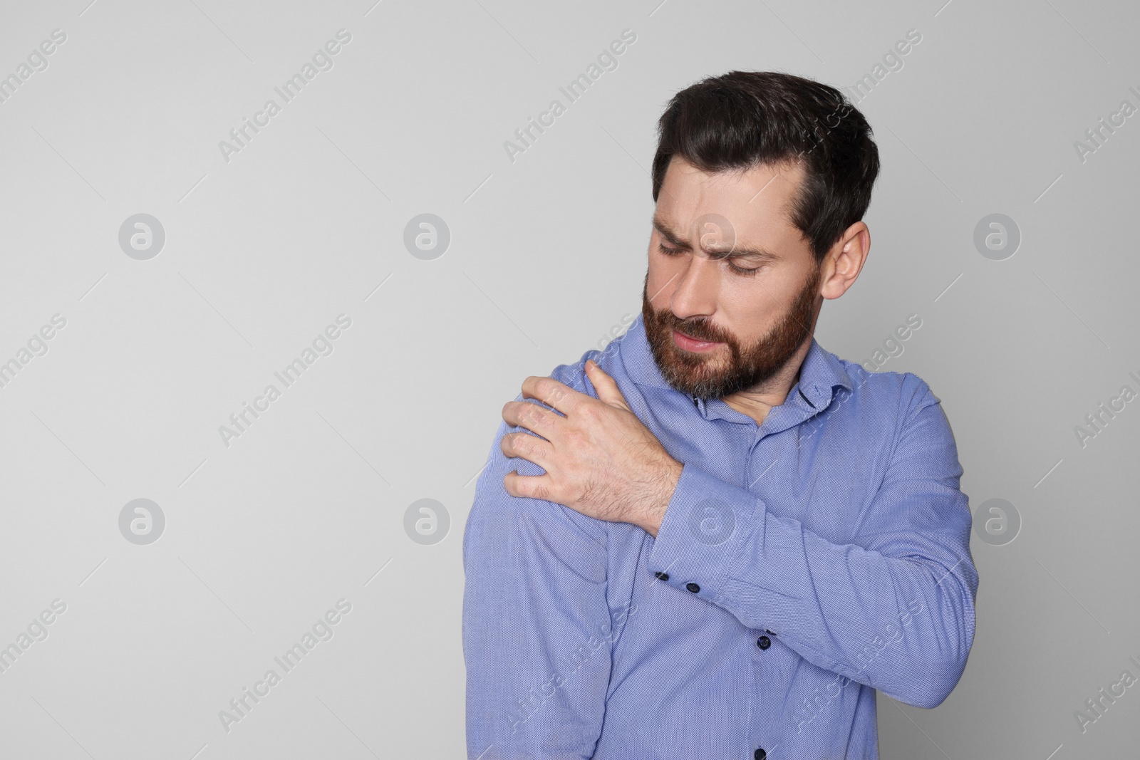 Photo of Man suffering from pain in his shoulder on light background, space for text. Arthritis symptoms