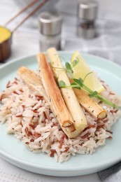 Photo of Plate with baked salsify roots, lemon and rice on table, closeup