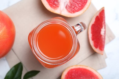 Photo of Tasty freshly made grapefruit juice on white marble table, flat lay