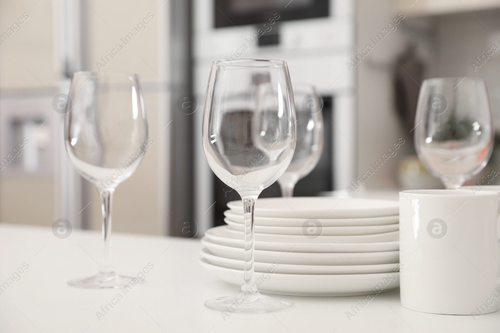 Photo of Stack of clean dishes, glasses and cup on table in kitchen