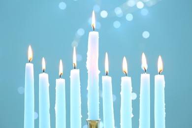 Photo of Hanukkah celebration. Burning candles on light blue background with blurred lights, closeup
