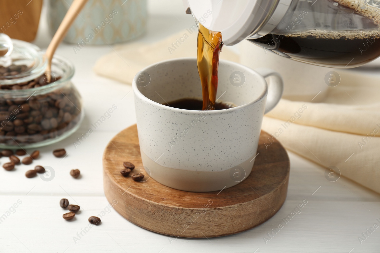 Photo of Pouring coffee into cup at white wooden table, closeup