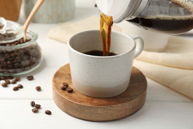 Photo of Pouring coffee into cup at white wooden table, closeup