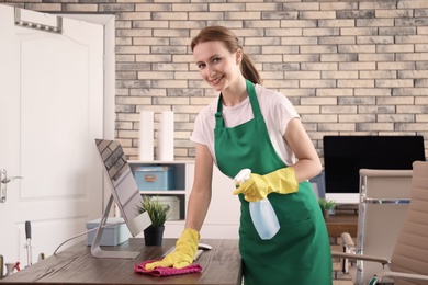 Photo of Young woman in apron and gloves cleaning office