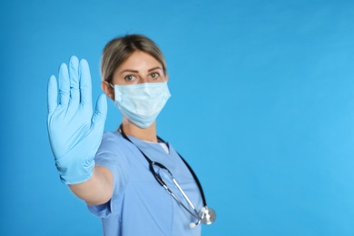 Photo of Doctor in protective mask showing stop gesture on light blue background, space for text. Prevent spreading of coronavirus