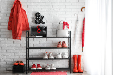 Photo of Shelving rack with stylish women's shoes and accessories near white brick wall indoors