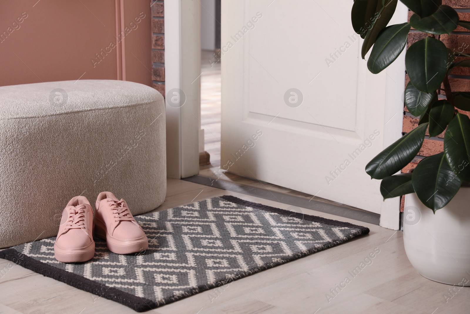 Photo of Hallway interior with beautiful houseplant, soft ottoman and door mat on floor near entrance