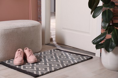 Hallway interior with beautiful houseplant, soft ottoman and door mat on floor near entrance