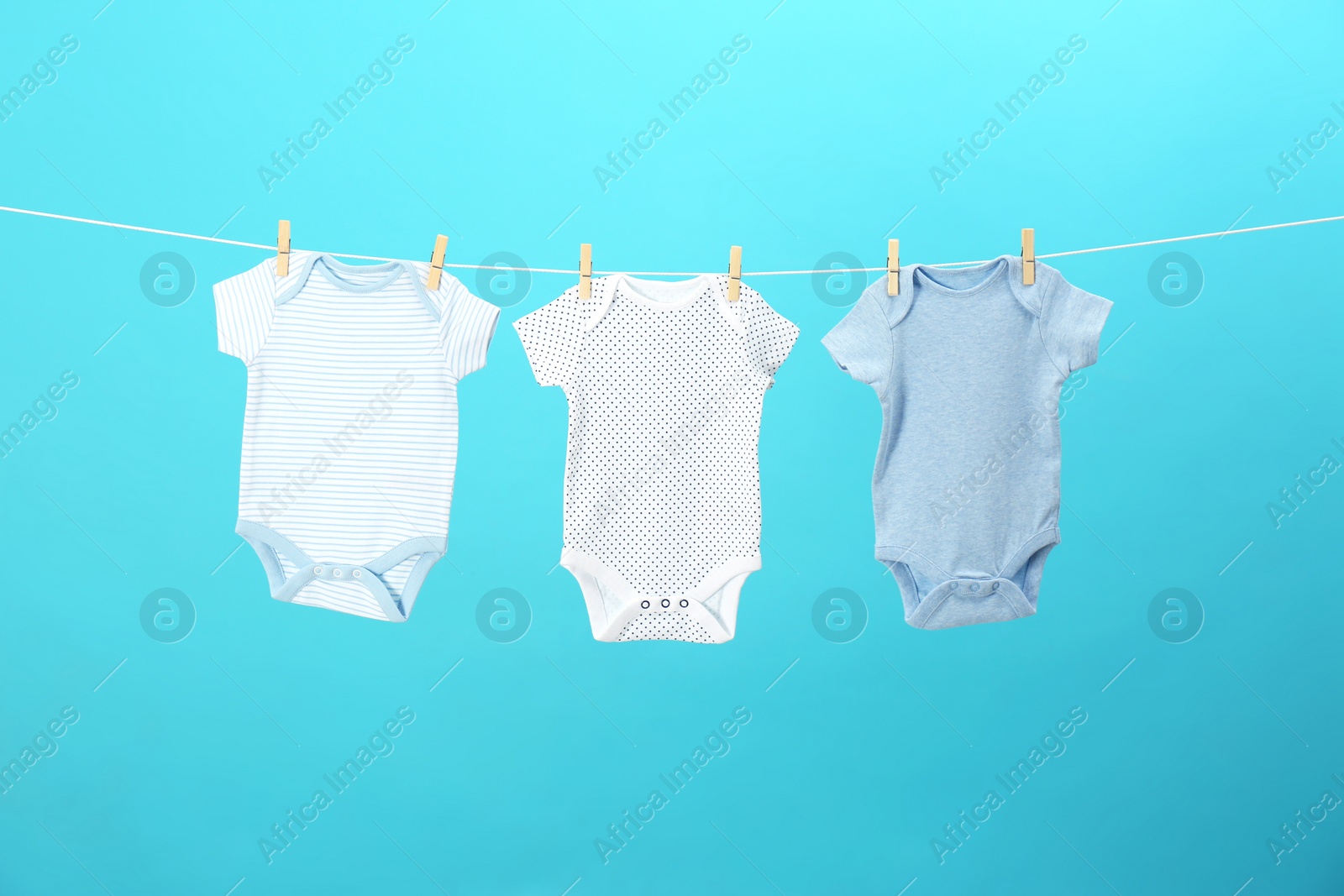 Photo of Colorful baby onesies hanging on clothes line against blue background. Laundry day