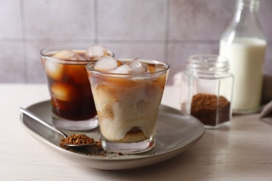 Photo of Refreshing iced coffee with milk in glasses, ingredients and spoon on light table, closeup