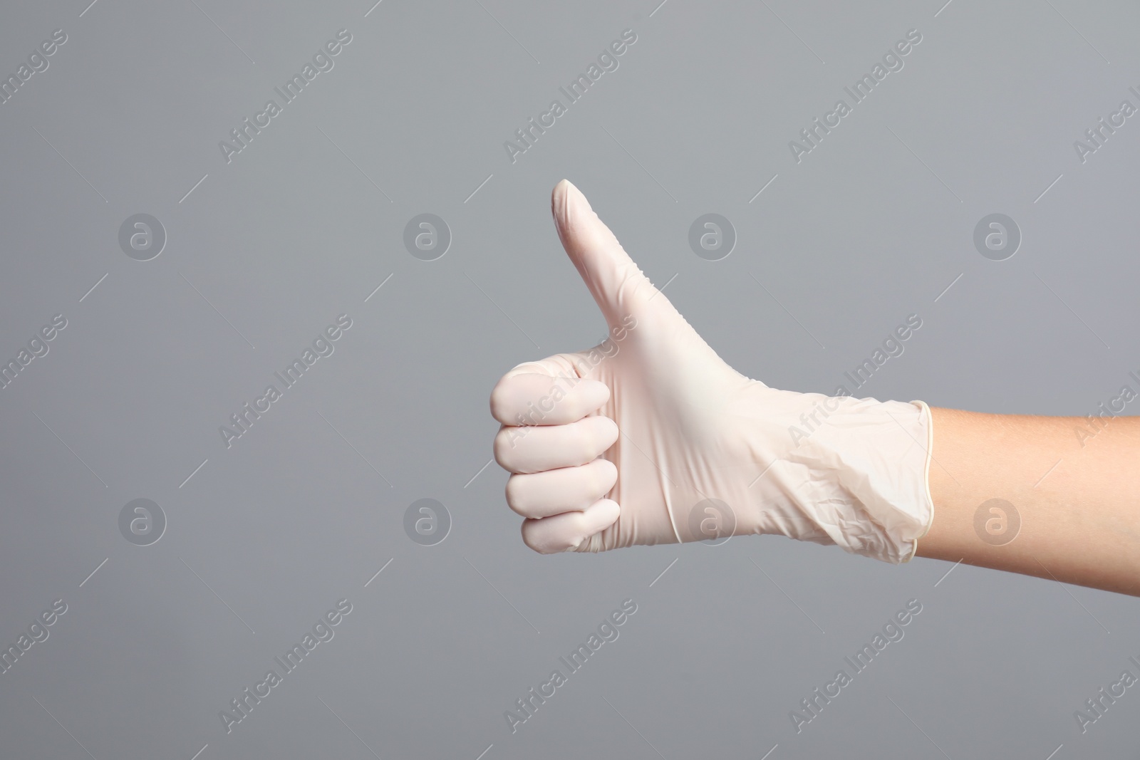 Photo of Doctor in medical gloves showing thumb up on grey background, closeup. Space for text