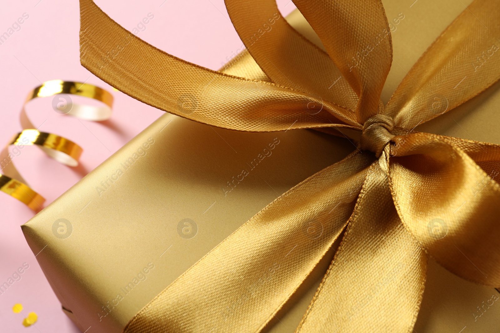 Photo of Golden gift box with bow on pink background, closeup