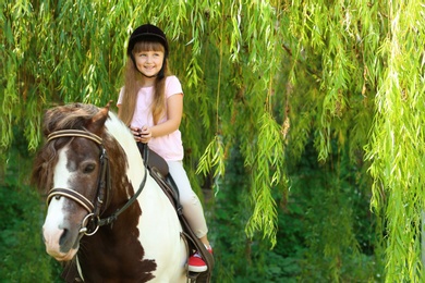 Photo of Cute little girl riding pony in green park