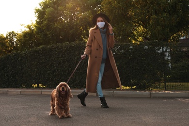 Woman in protective mask with English Cocker Spaniel outdoors. Walking dog during COVID-19 pandemic