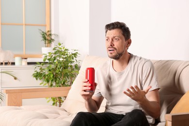 Photo of Disappointed man with can of beverage on sofa indoors
