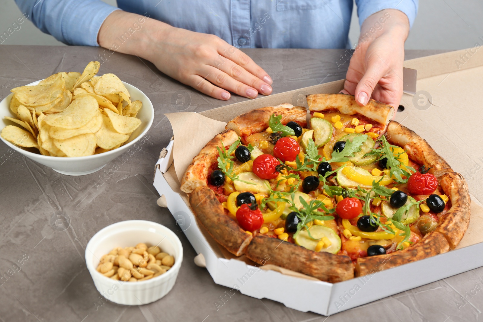 Photo of Woman taking slice of delicious vegetable pizza at grey table, closeup