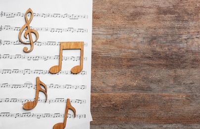 Photo of Music notes with sheet on wooden background, flat lay. Space for text