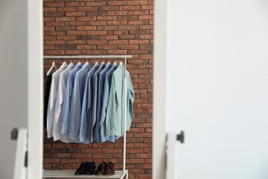 Photo of Reflection of wardrobe rack with men's clothes near brick wall in mirror at home. Space for text