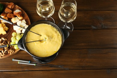 Photo of Fondue pot with melted cheese, glasses of wine and different products on wooden table, flat lay. Space for text