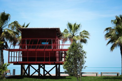 Red wooden lifeguard house and palm trees on seacoast