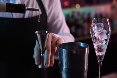Cocktail making. Bartender pouring alcohol from bottle into jigger on blurred background, closeup