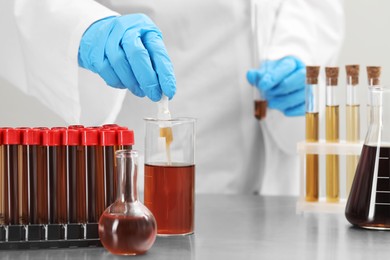Photo of Scientist taking brown liquid with pipette from beaker at table, closeup