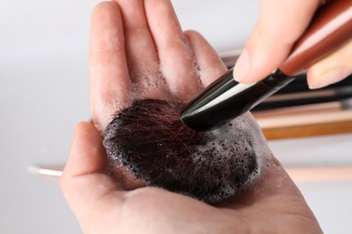 Photo of Woman washing makeup brush with soap, closeup