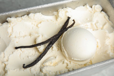 Photo of Container with delicious ice cream and vanilla pods on table, closeup