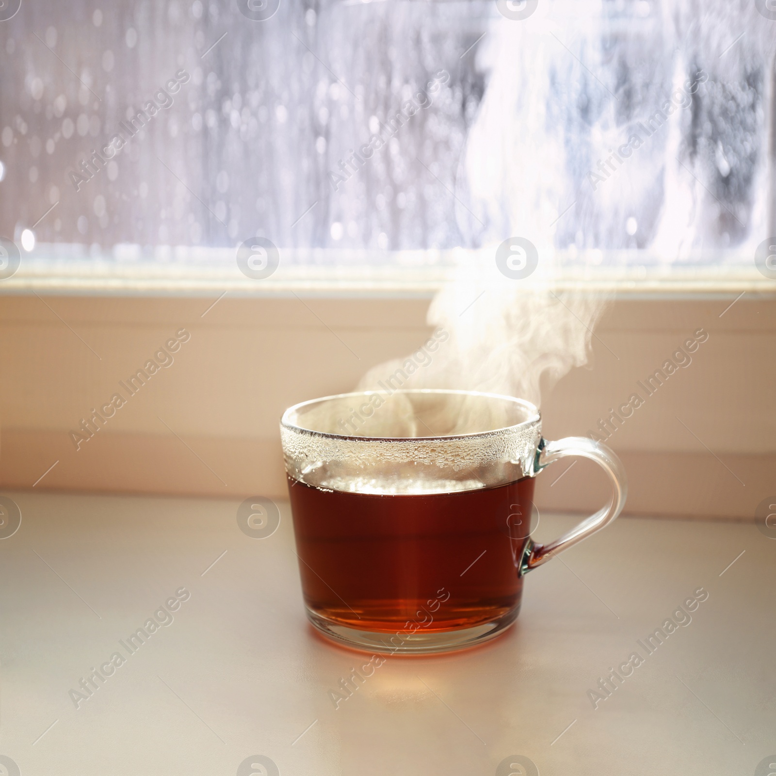 Photo of Cup of hot tea near window on rainy day