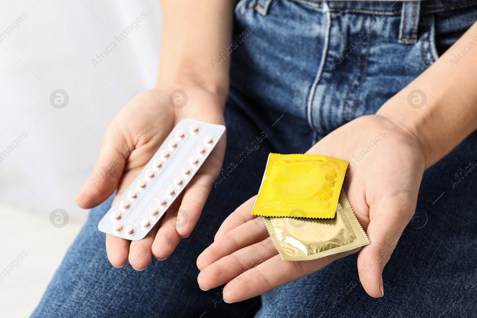 Photo of Young woman holding birth control pills and condoms on light background, closeup. Safe sex concept