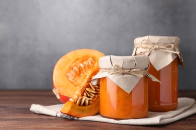 Photo of Jars of pumpkin jam and fresh pumpkin on wooden table