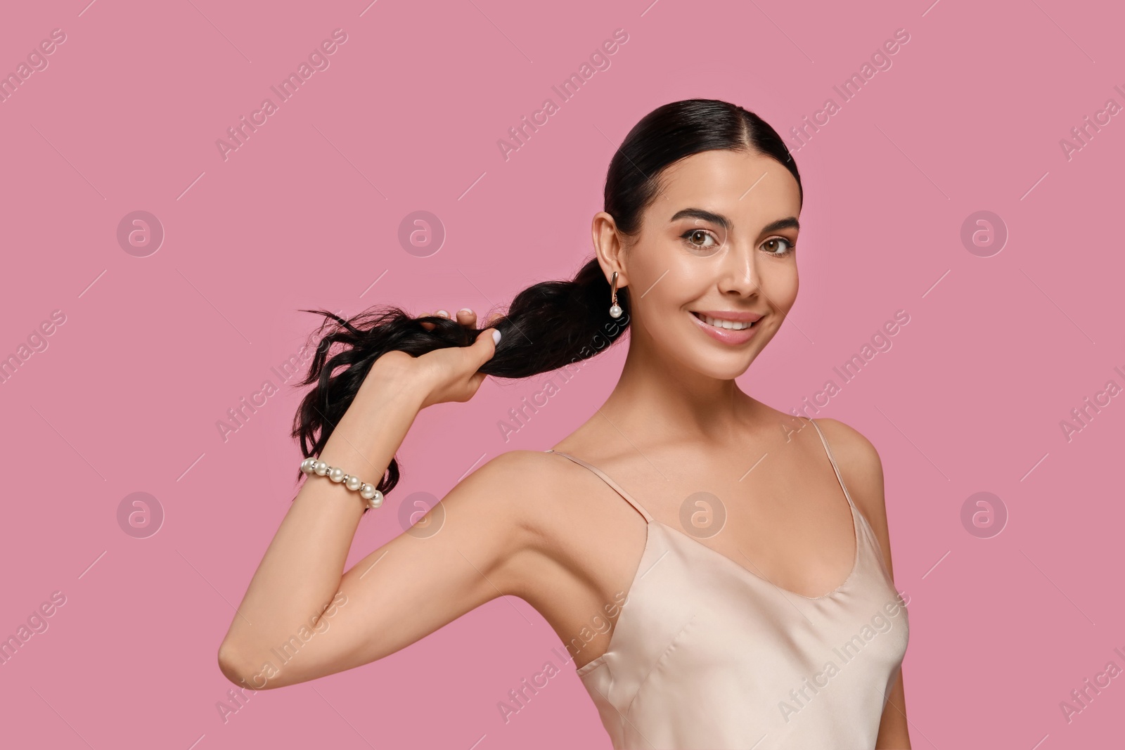 Photo of Young woman wearing elegant pearl jewelry on pink background