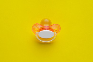 New baby pacifier on yellow background, top view