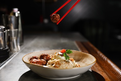 Photo of Chopsticks with meat ball over plate of rice on table indoors