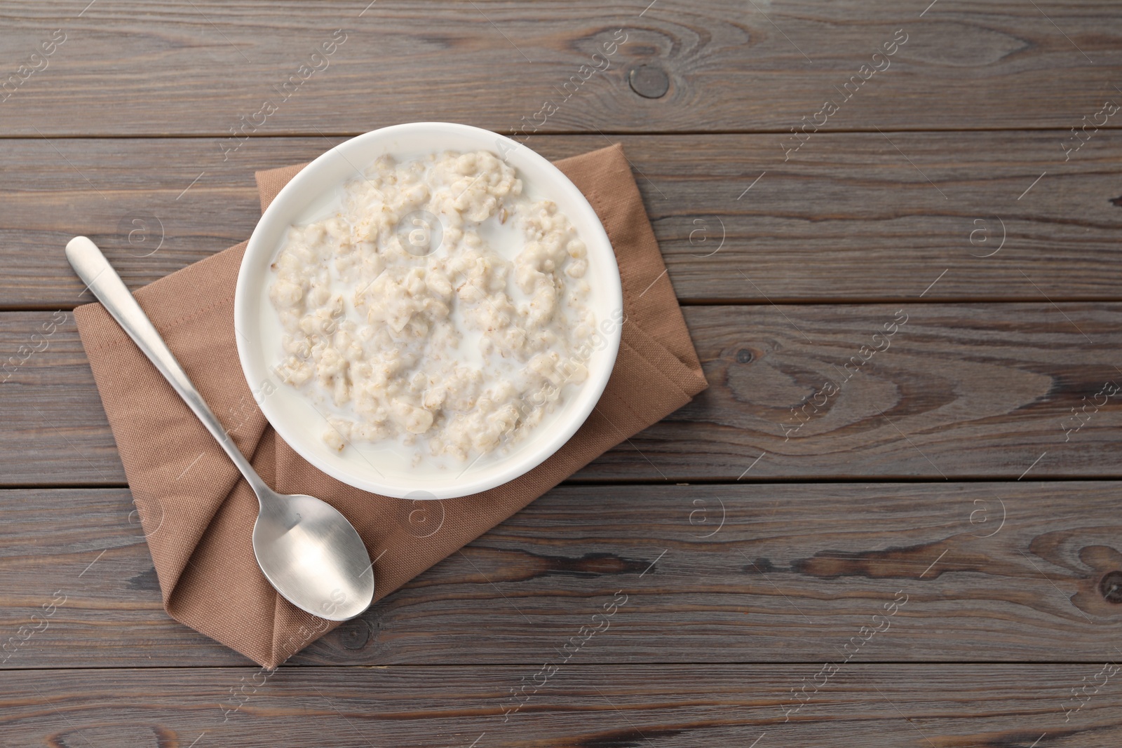 Photo of Tasty boiled oatmeal in bowl and spoon on wooden table, top view. Space for text