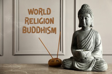 Buddha statue, incense sticks on grey table and text World Religion Buddhism