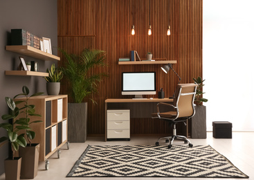 Comfortable workplace with computer near wooden wall in stylish room interior. Home office design