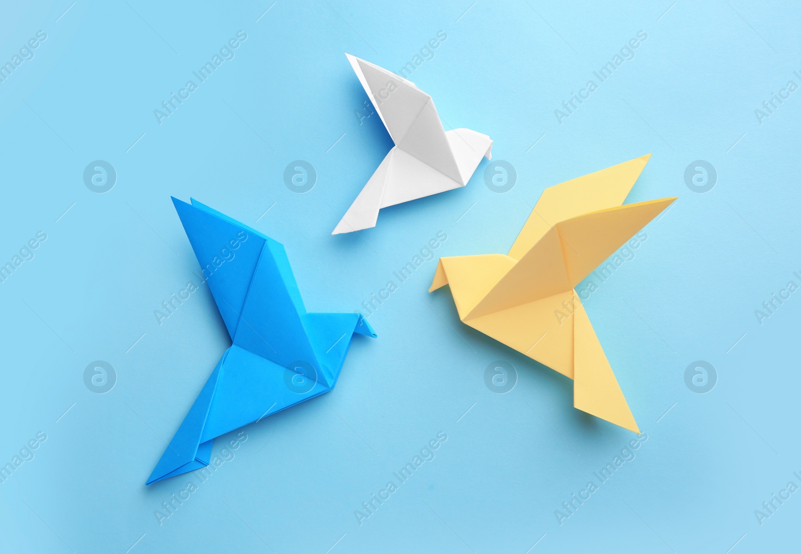 Photo of Origami art. Colorful handmade paper birds on light blue background, flat lay