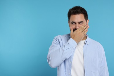 Photo of Embarrassed man covering mouth on light blue background. Space for text