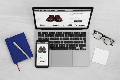 Photo of Online store website on laptop screen. Computer, smartphone, stationery and glasses on light grey wooden table, flat lay