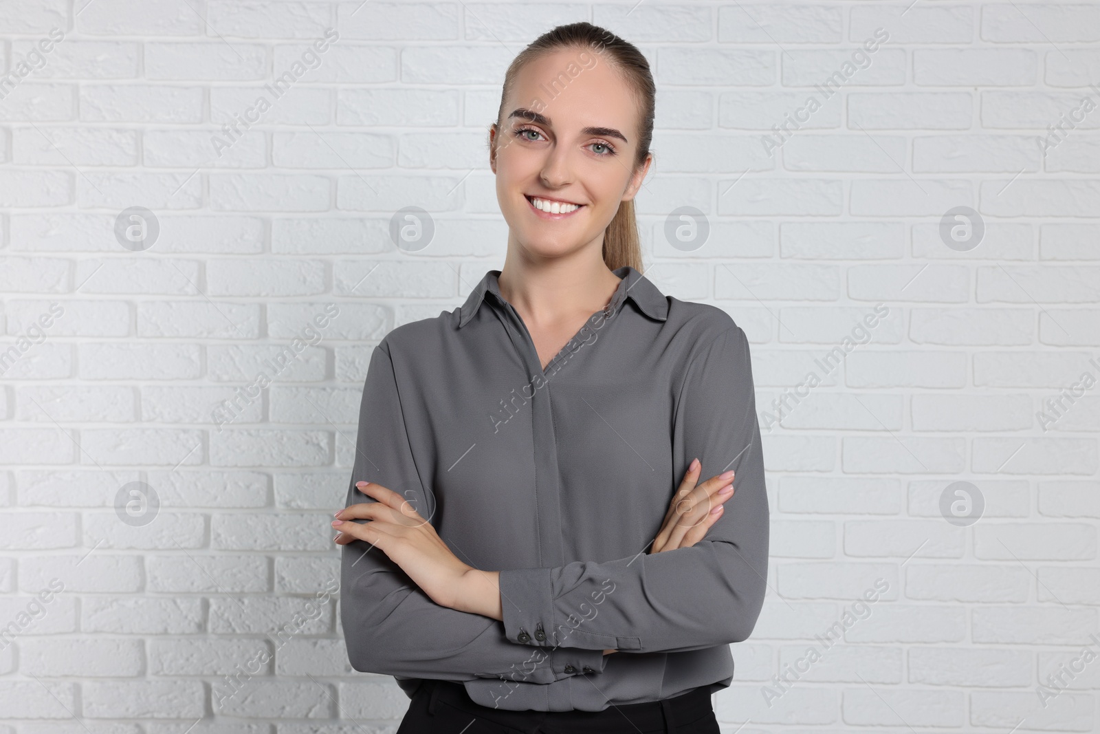 Photo of Happy young secretary with crossed arms near white brick wall