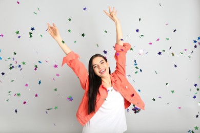 Photo of Happy woman and falling confetti on light grey background