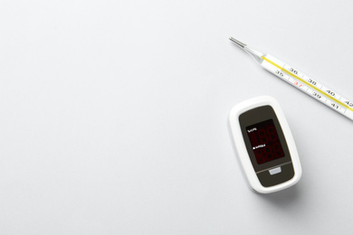 Modern fingertip pulse oximeter and mercury thermometer on white background, flat lay. Space for text
