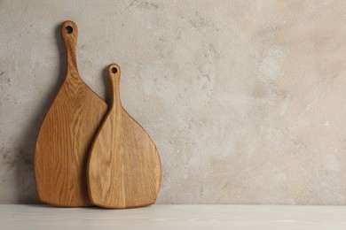 Photo of Wooden cutting boards on white table near textured wall, space for text