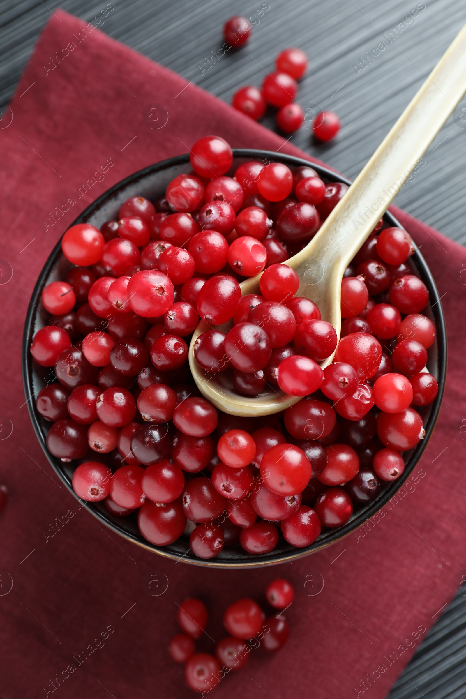 Photo of Cranberries in bowl and spoon on black wooden table, top view